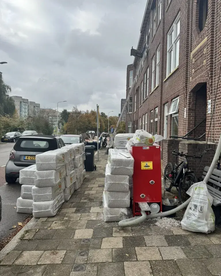 Inblaasmachine en zakken cellulose op de stoep voor een rij oude stadswoningen