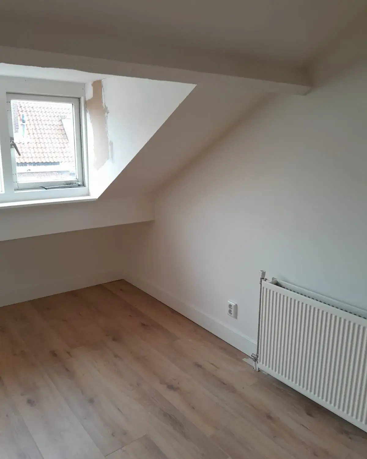 Opgeleverde zolderkamer met een glad wit schuin plafond en een dakraam