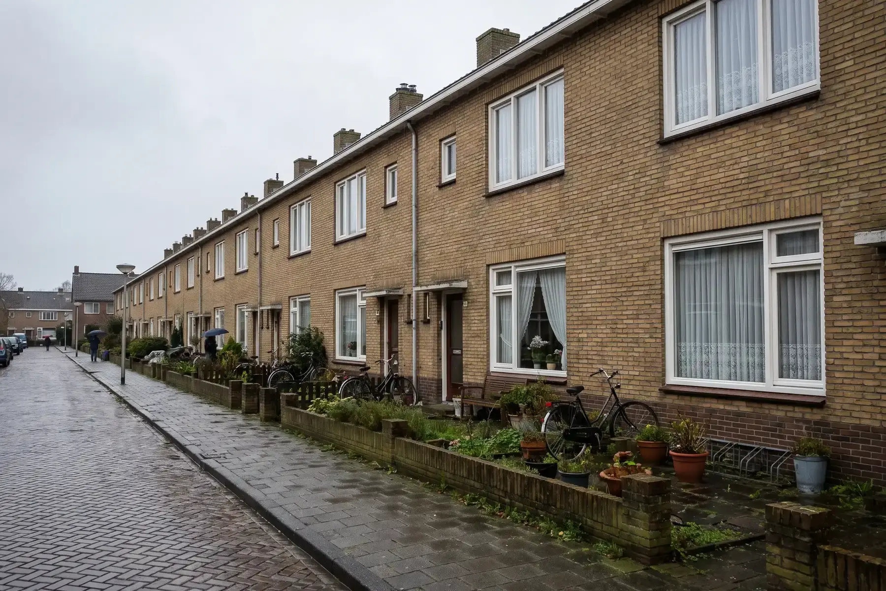 Rij naoorlogse rijtjeswoningen van gele baksteen in een lange rechte straat