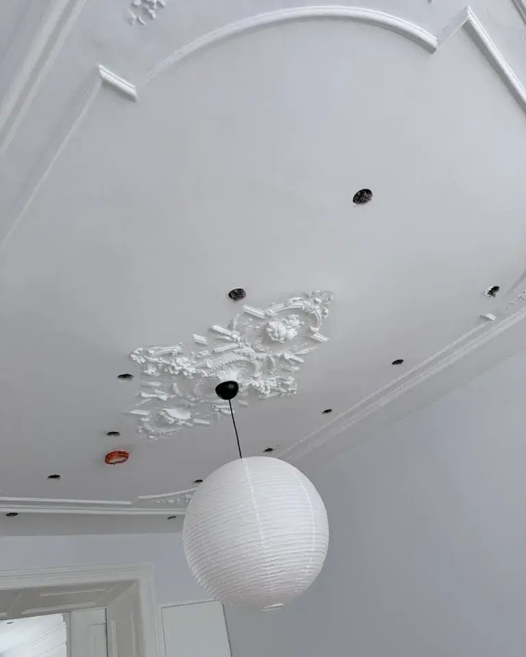 Oud stucplafond met een sierrozet en een paar open boorgaten vóór het dichtzetten